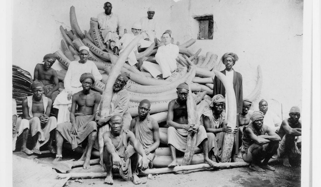 Ernst Moore, a Connecticut ivory trader, poses among Arab and Indian merchants and African caravan tusk porters in Zanzibar around 1900.